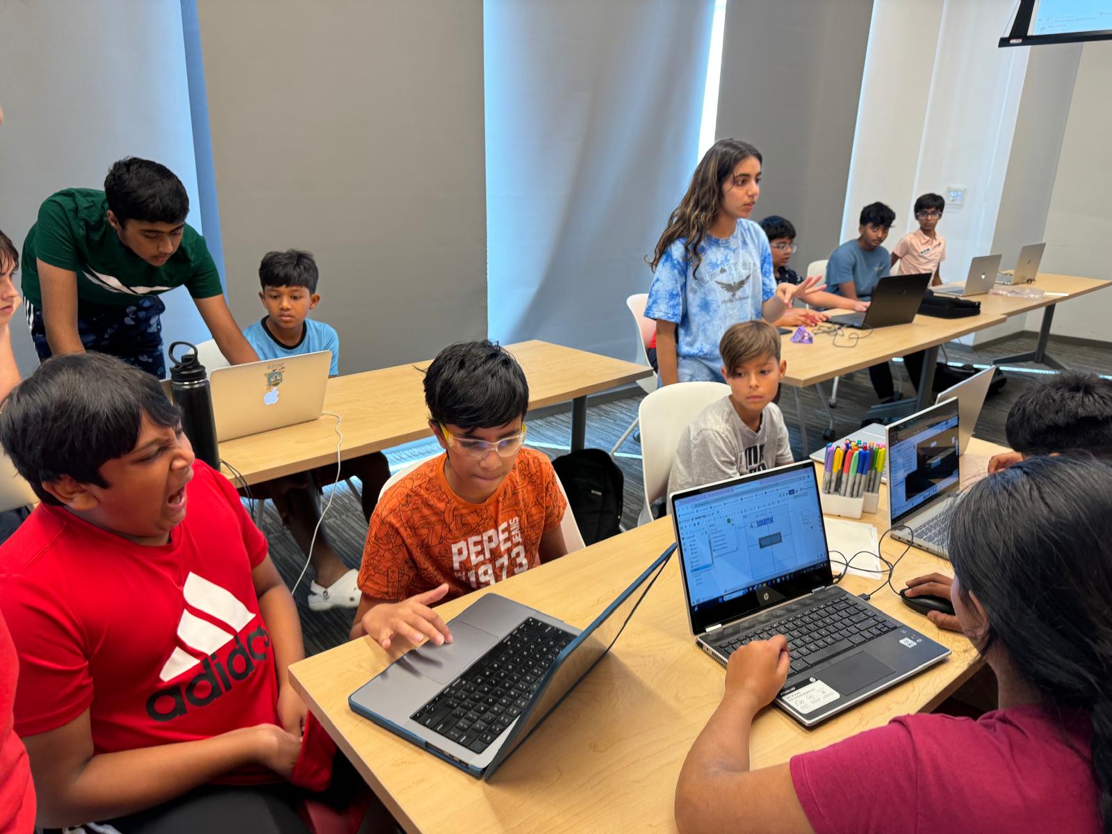 Students collaborate in small groups while creating CAD models on laptops.
