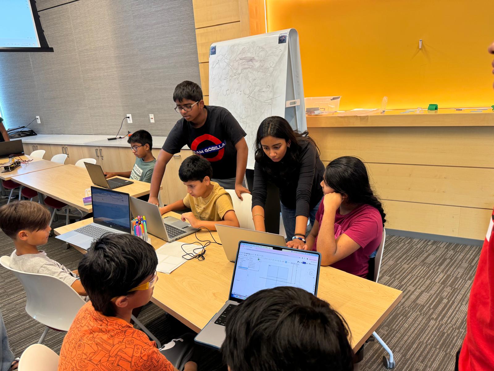 Student mentors support younger learners working on CAD designs at laptop computers.