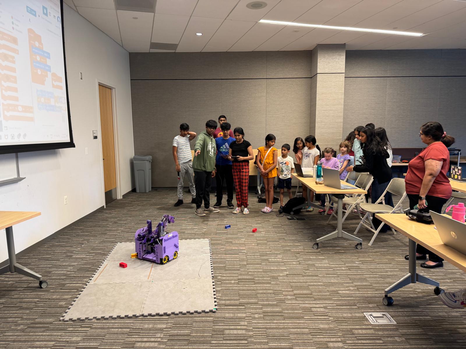 Students watch a purple competition robot demonstrate its movement during a Girls in Robotics program.