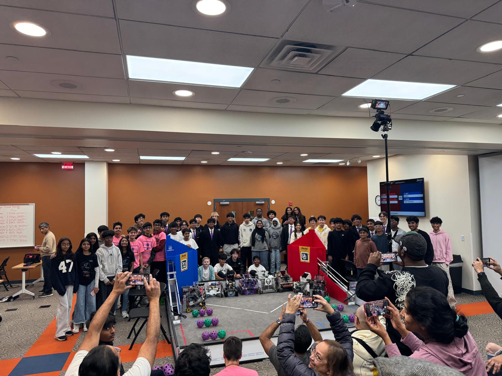 Students, mentors, teams, and families gather around an FTC competition field after a robotics scrimmage.