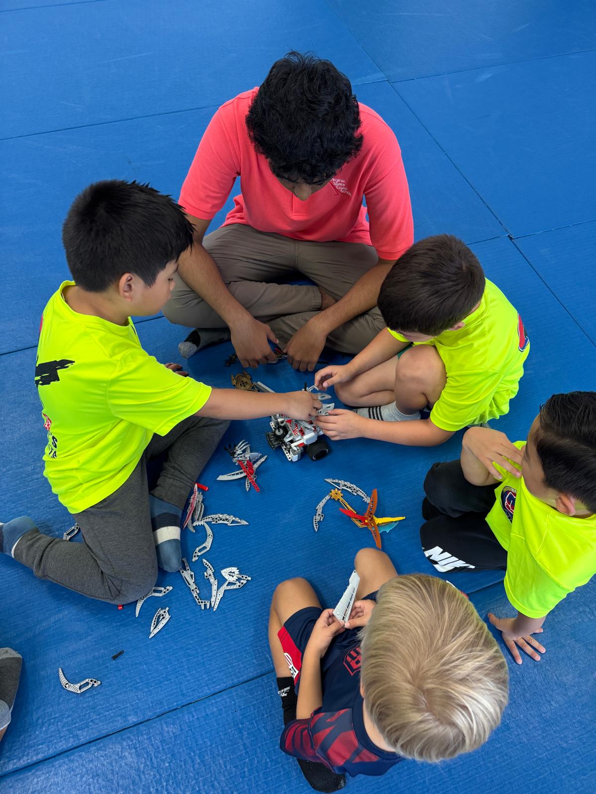 A mentor and students work together to assemble and test a small robot during summer camp.